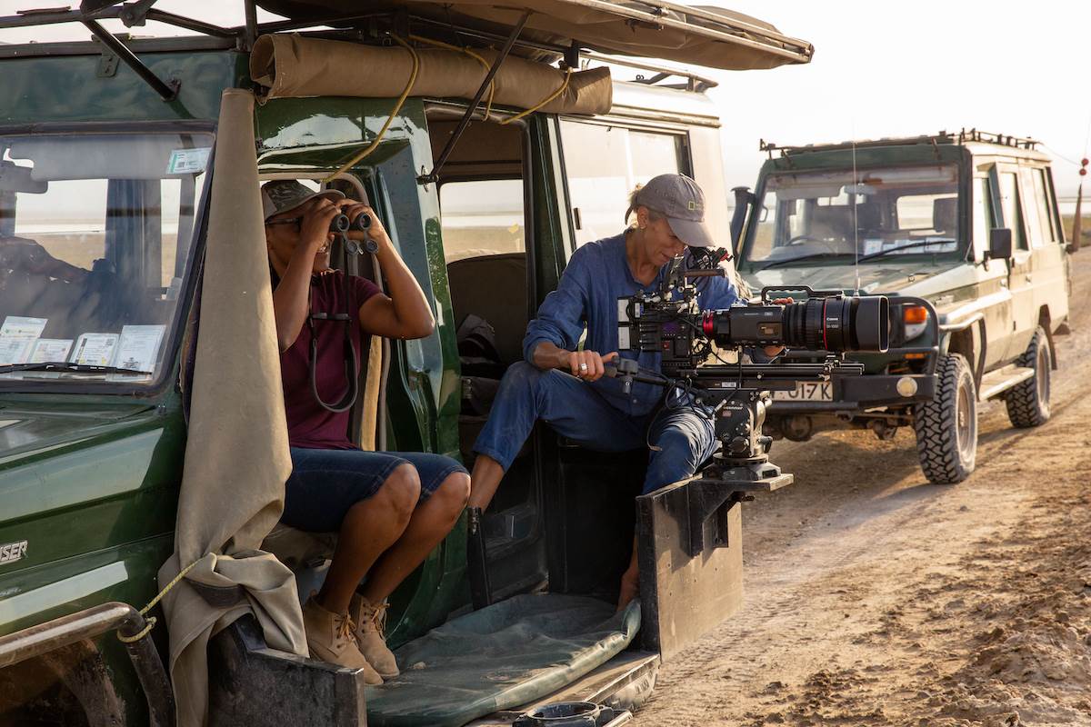 Series Director and Mentee Faith Musembi looks through binoculars as Queens SeriesDirector of Photography Sophie Darlington films from a vehicle. (National Geographicfor Disney/Rachael Kinley