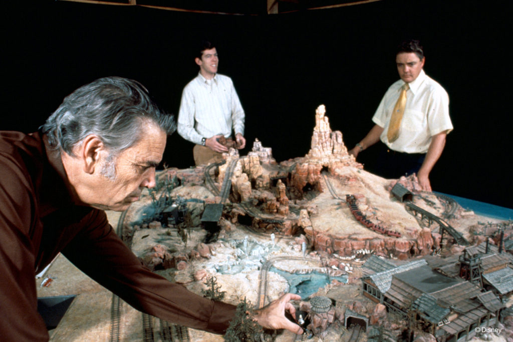 THE WILDEST RIDE IN THE WILDERNESS –– (Left to right) Imagineers Claude Coats, Tony Baxter, and David Schweninger review a model of Big Thunder Mountain Railroad for Magic Kingdom park at Walt Disney World. Originally designed for the Florida resort, the attraction first opened at Disneyland park in 1979 and later inspired versions at Tokyo Disneyland and Disneyland Paris. (Disney)