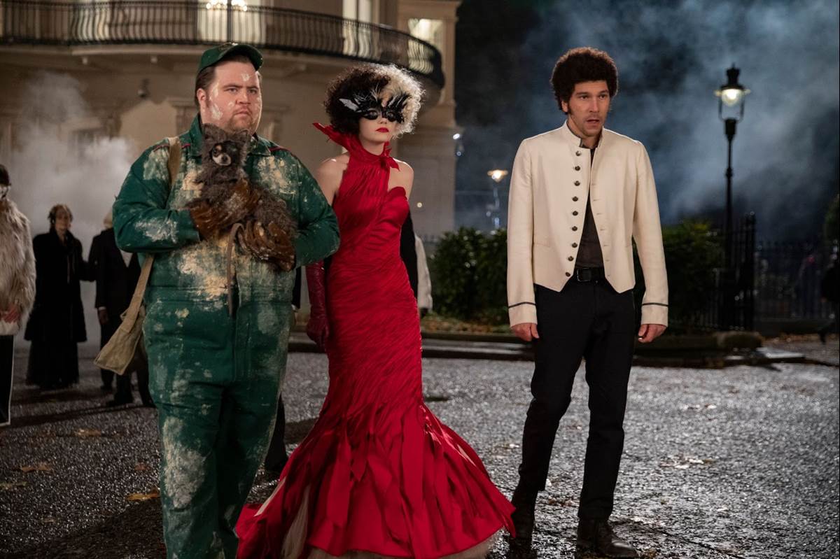 (L-R): Paul Walter Hauser as Horace, Emma Stone as Cruella and Joel Fry as Jasper in Disney’s live-action CRUELLA. Photo by Laurie Sparham. © 2021 Disney Enterprises Inc. All Rights Reserved.